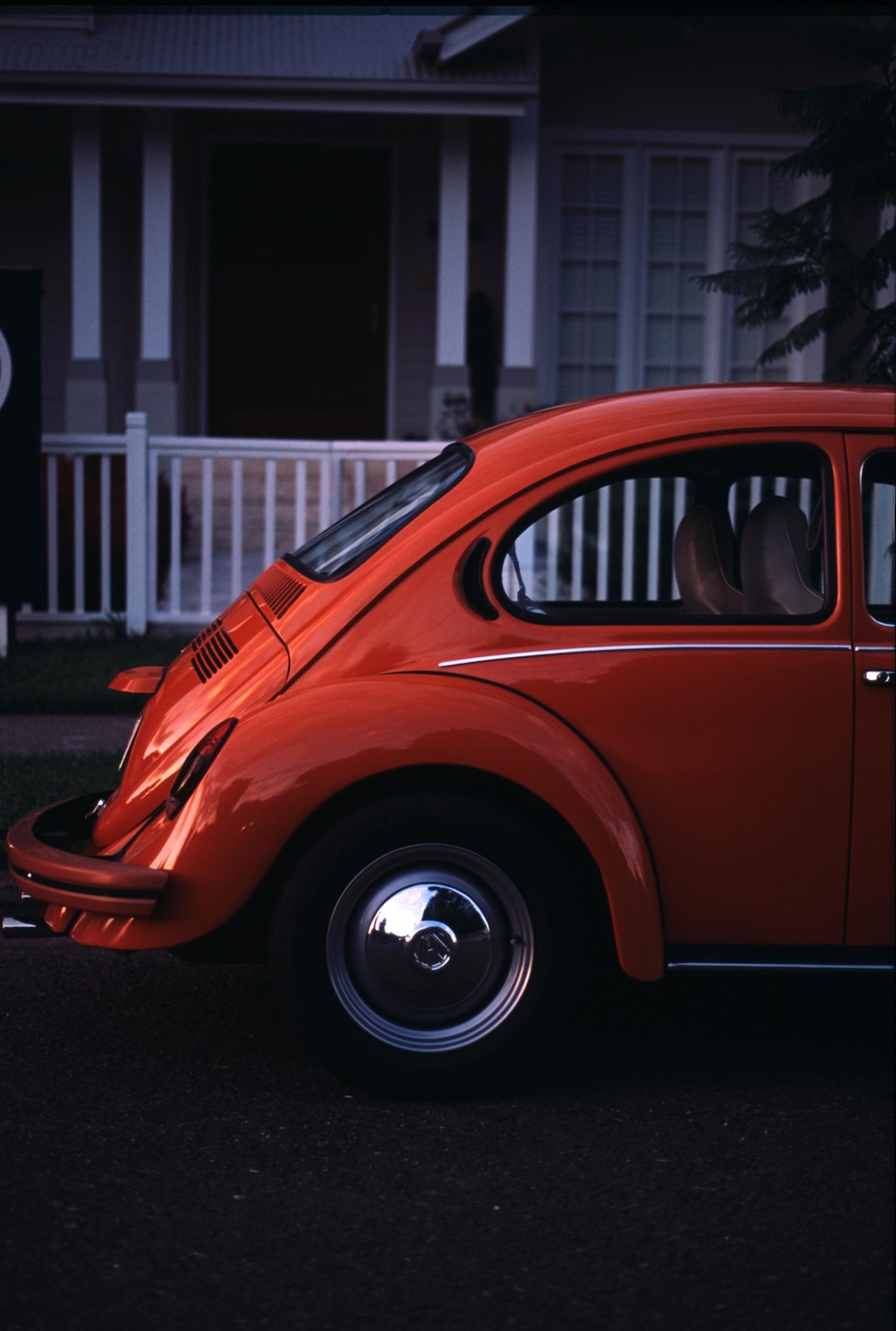 A red Volkswagen Beetle is parked in front of a house with a white porch railing.