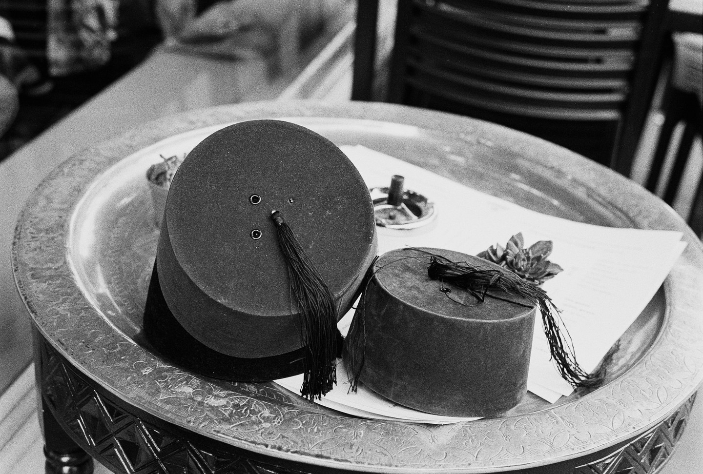 Two fezzes with tassels rest on a decorative metal tray with an ashtray and paper.