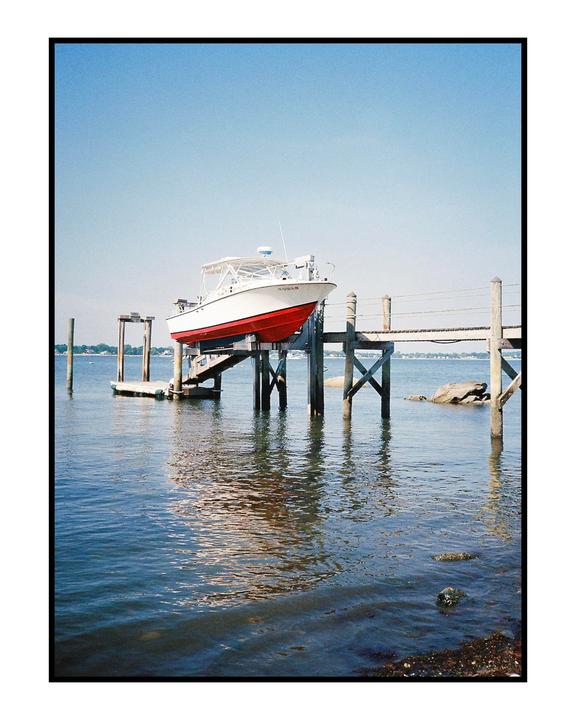 A white and red boat is docked on a wooden pier over calm water under a clear sky.