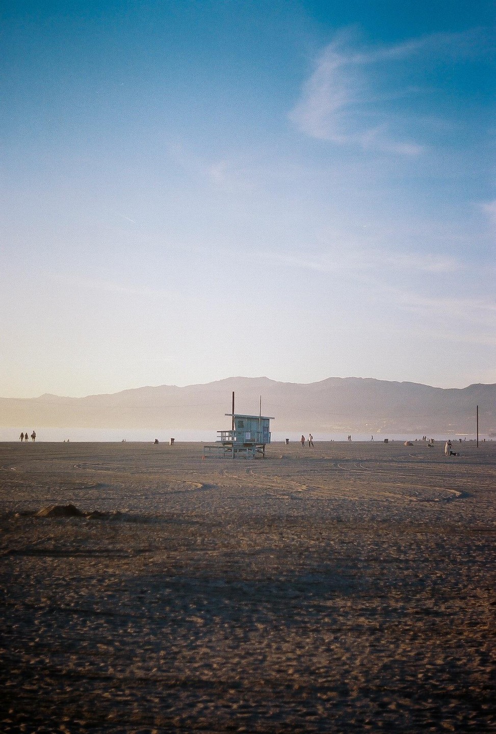 A lifeguard stand sits on a wide, sandy beach with mountains in the distance under a clear sky.
