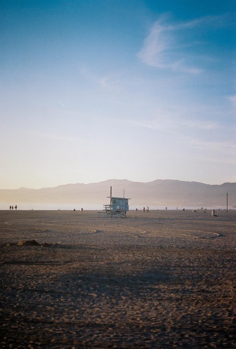 A lifeguard stand sits on a wide, sandy beach with mountains in the distance under a clear sky.