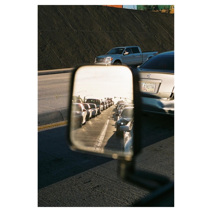 A car's side mirror reflects a line of cars in traffic on a highway.