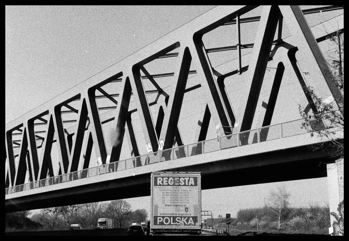 A truck with "Regesta Polska" written on its back drives under a bridge with a geometric design.