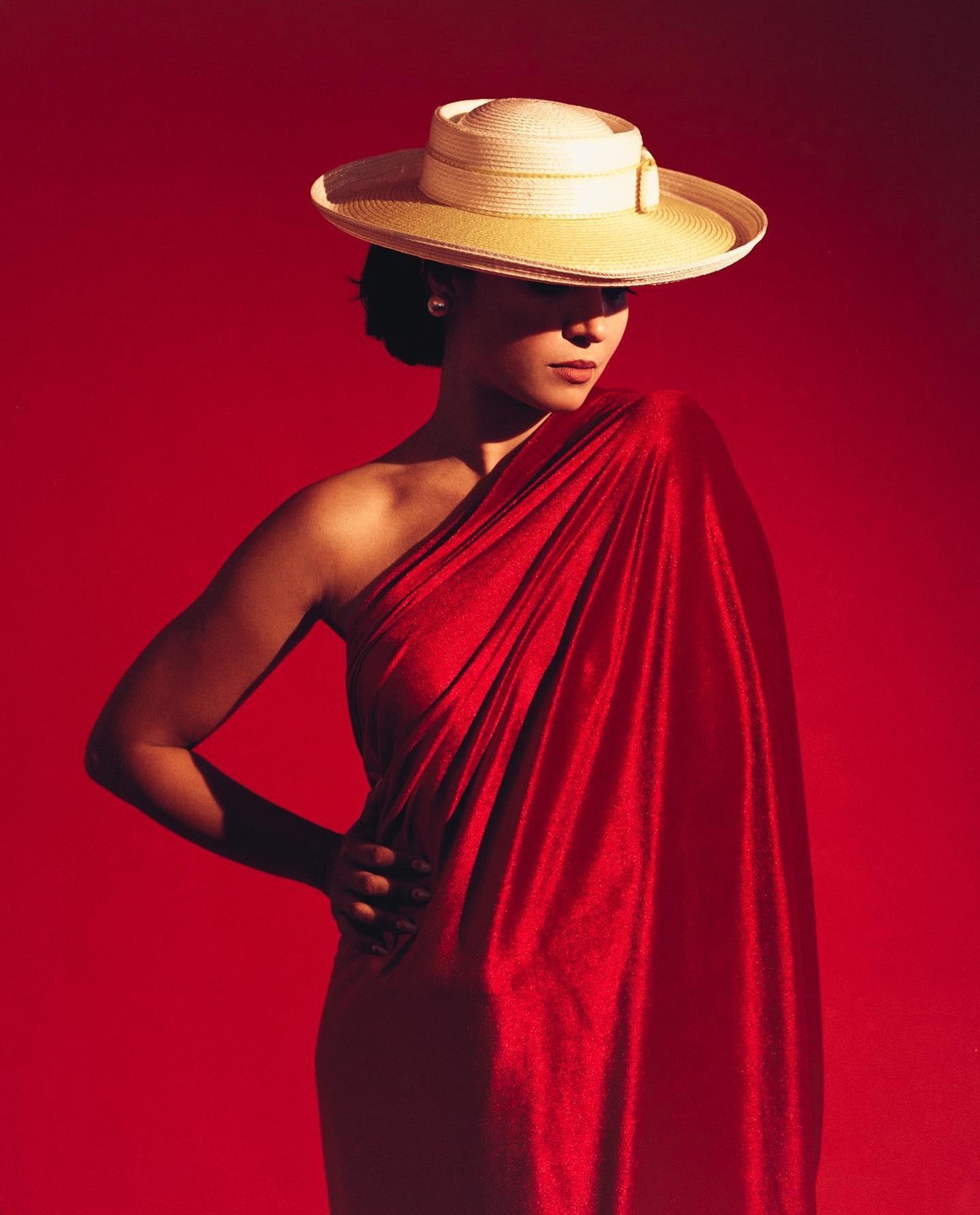 A woman in a red dress and a straw hat poses against a red background.