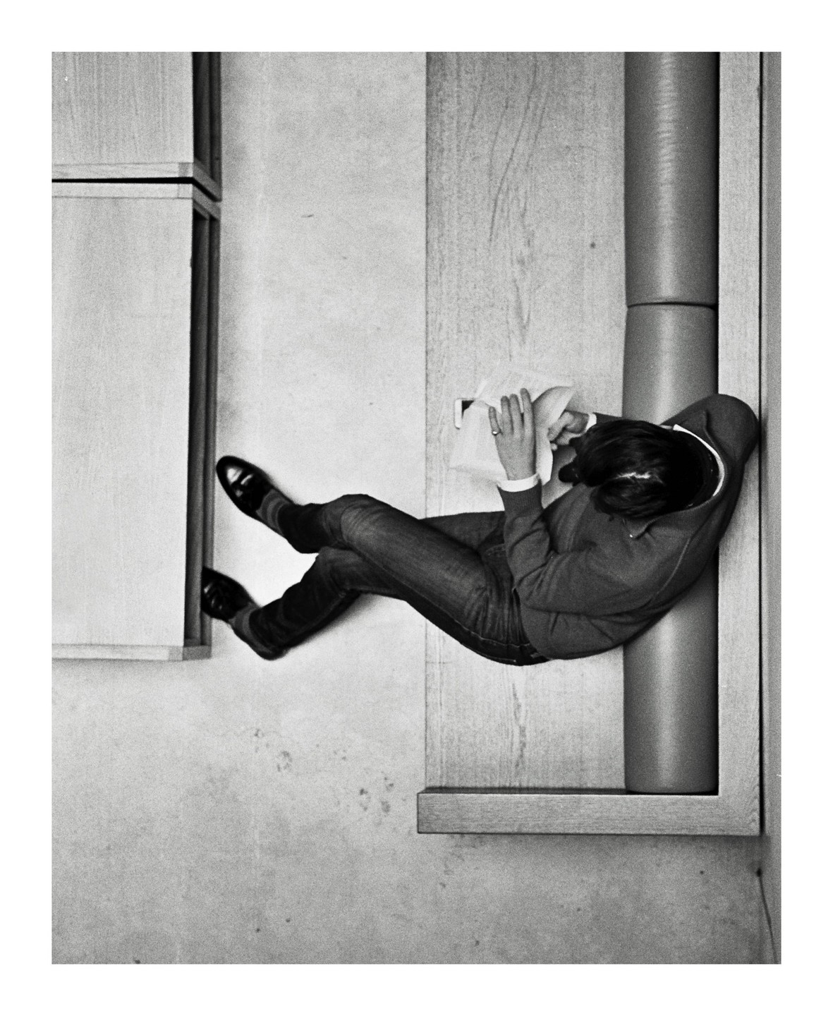 A woman wearing jeans and a sweater is lying down and reading a book in a museum.