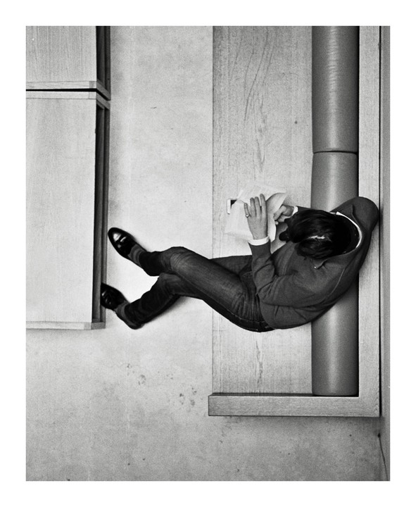 A woman wearing jeans and a sweater is lying down and reading a book in a museum.
