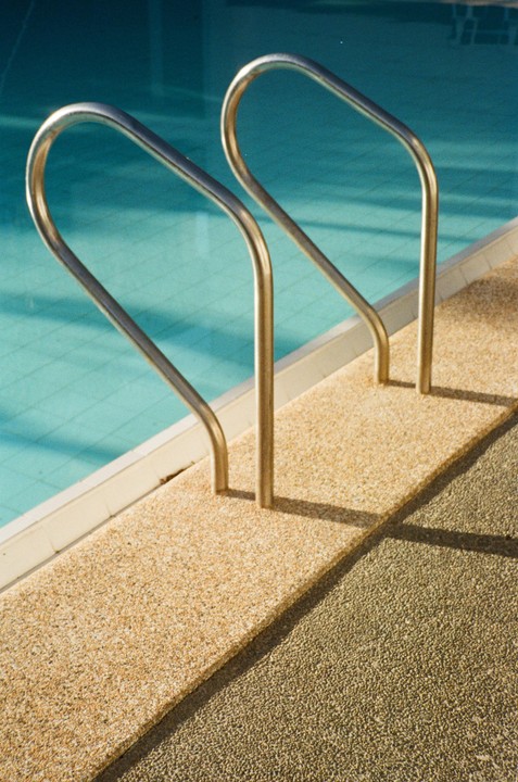 Two metal handrails extend into a swimming pool from a textured concrete deck.