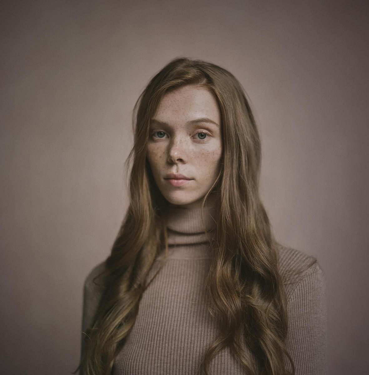 A woman with long, wavy hair and freckles looks directly at the viewer.