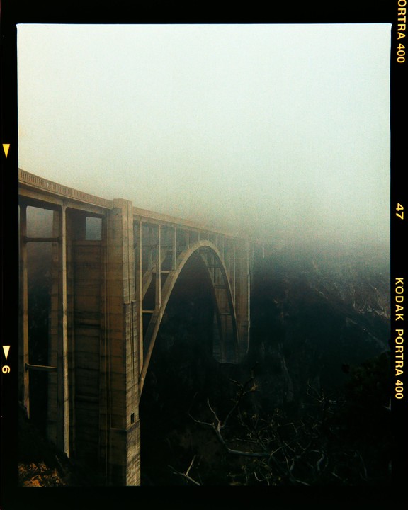 A large concrete bridge with arches extends into a thick fog.