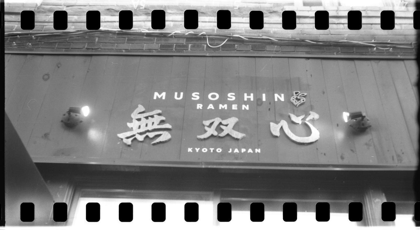 A black and white photograph shows the sign for Musoshin Ramen in Kyoto, Japan.