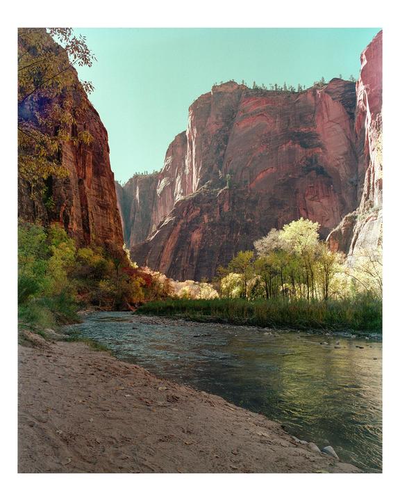 A river flows through a canyon with tall rock walls and trees with autumn foliage.
