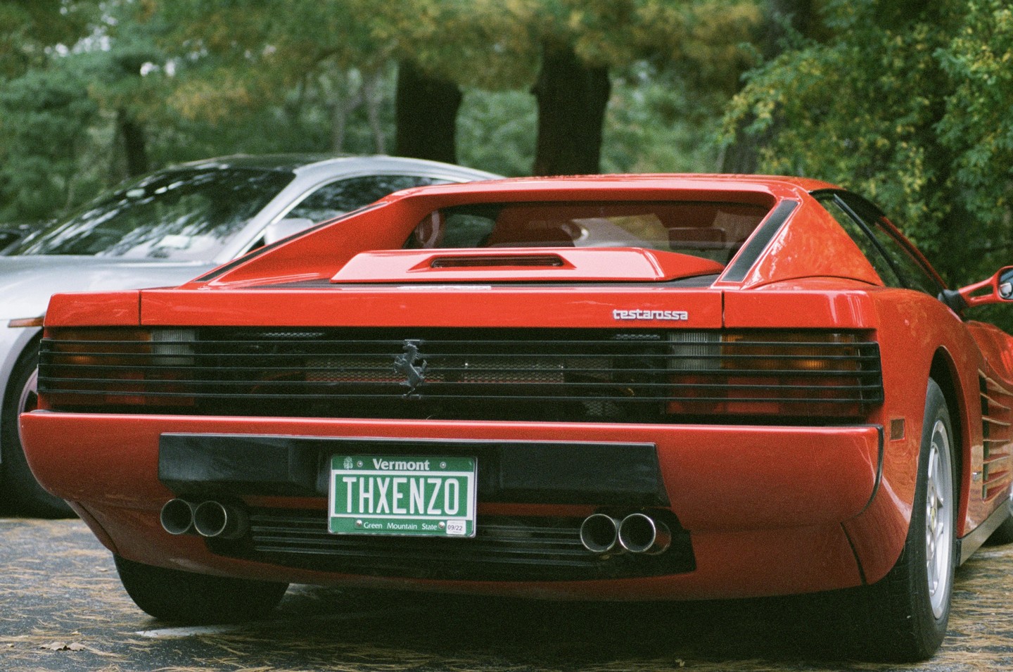 The rear of a red Ferrari Testarossa with a Vermont license plate is parked outdoors.