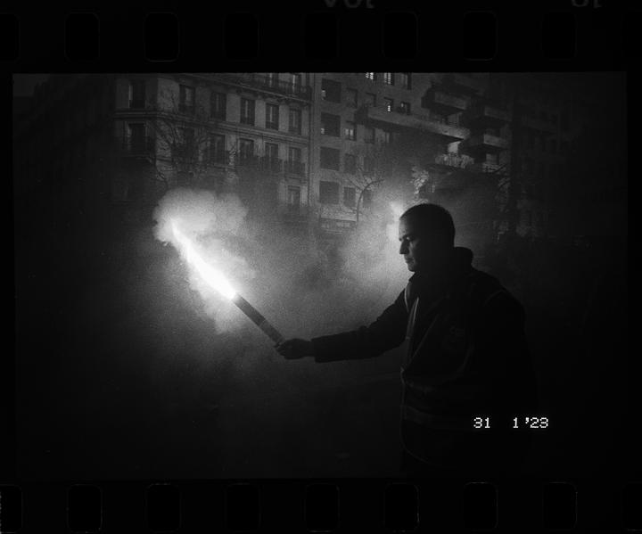A man holds a flare that illuminates his face and the street at night.