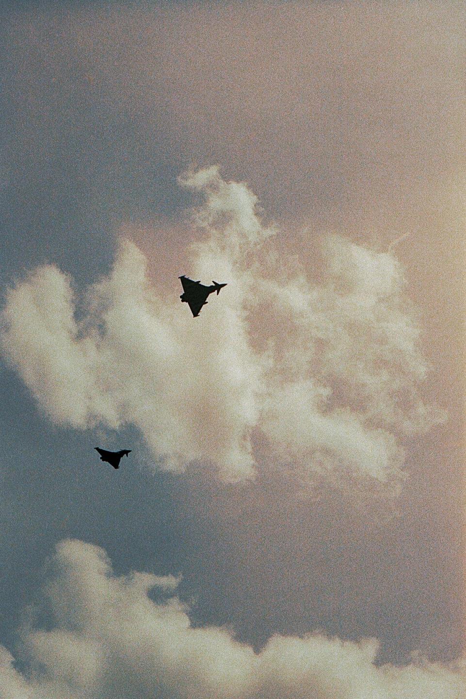 Two fighter jets are silhouetted against a cloudy sky.