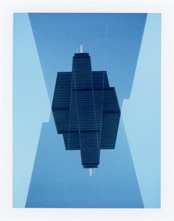 A double exposure shows the Willis Tower reflected and inverted against a blue sky.