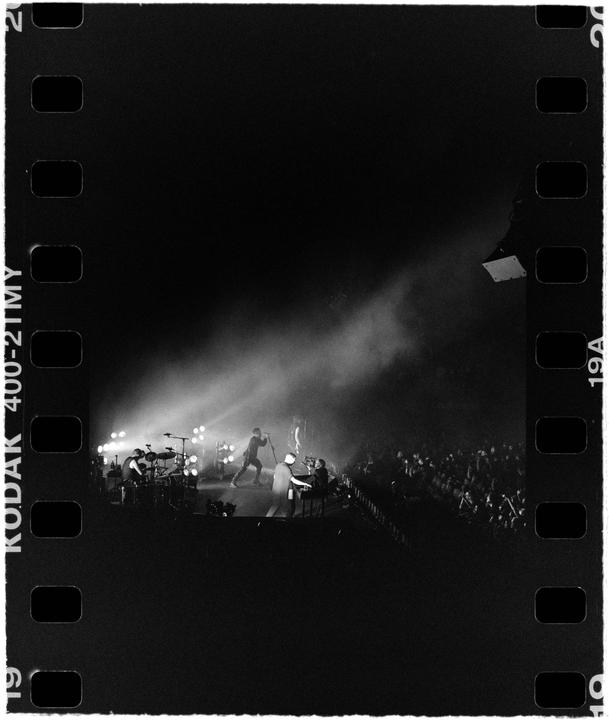 A band performs on a stage illuminated by spotlights in front of a large crowd.