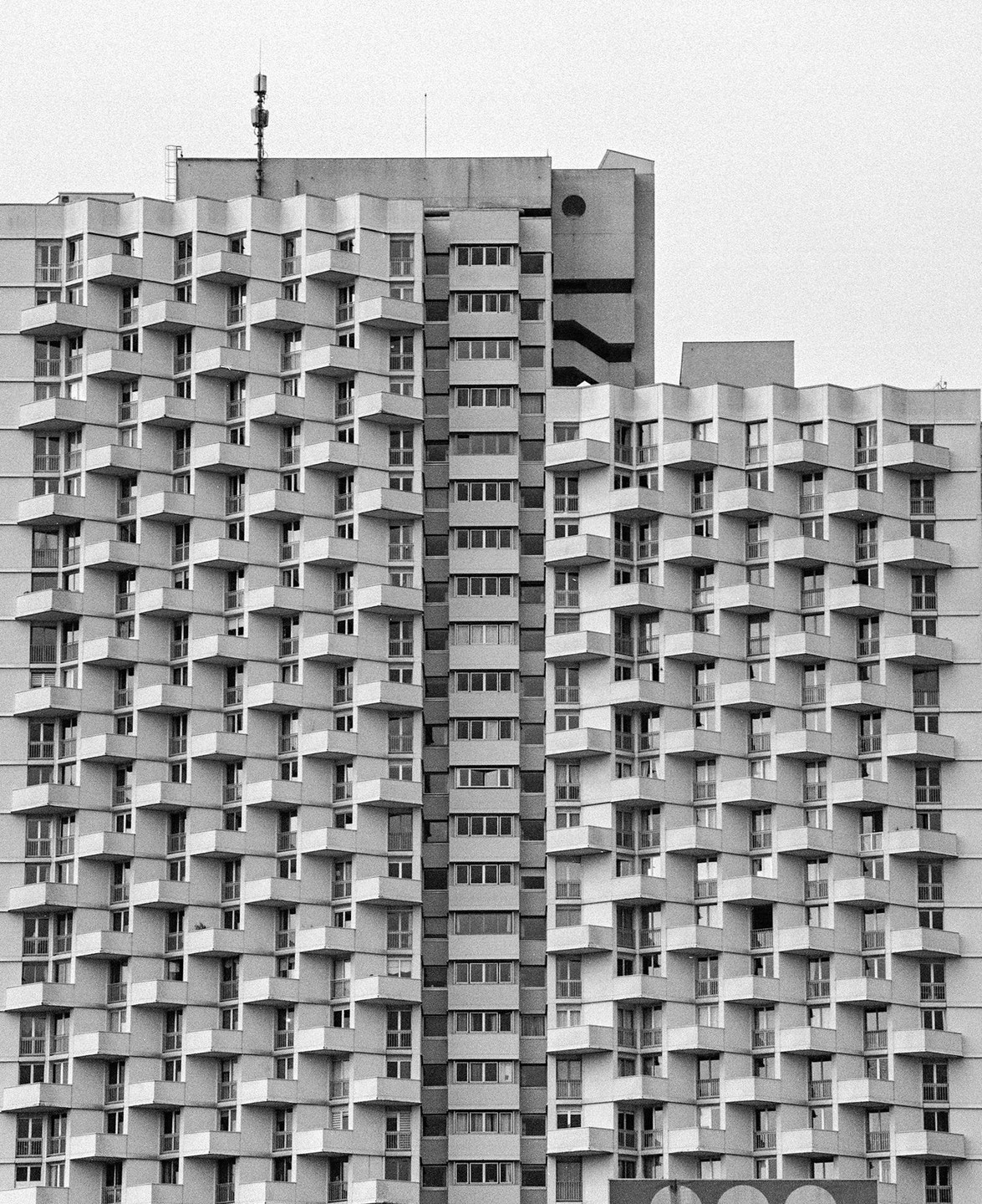 A tall building with a complex facade of balconies and windows stands against a plain sky.