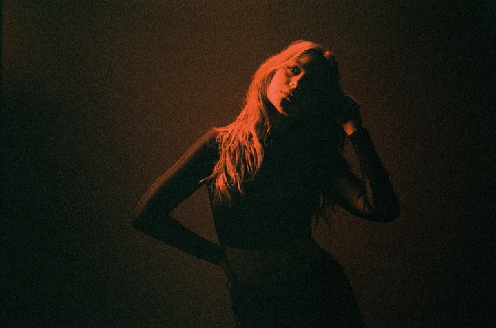 A woman with long hair is illuminated by red light in a dark room.