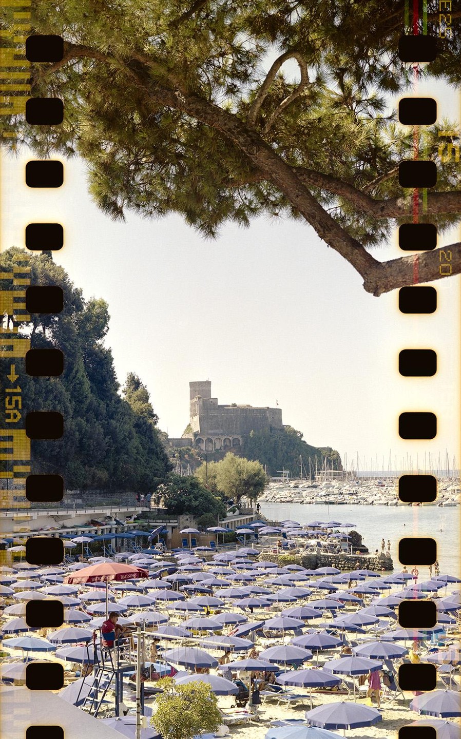 A beach with many blue umbrellas and people is visible, with a castle and a harbor full of boats in the background.