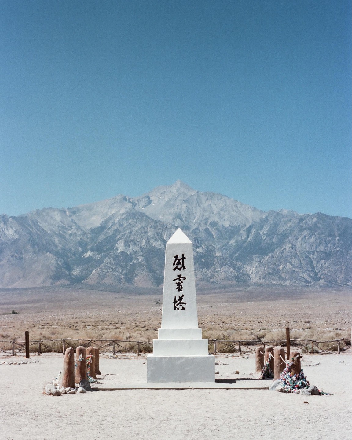 A white obelisk with Japanese characters stands in a desert landscape with mountains in the background.