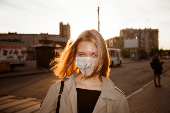 A woman wearing a face mask looks directly at the camera during golden hour on a street.