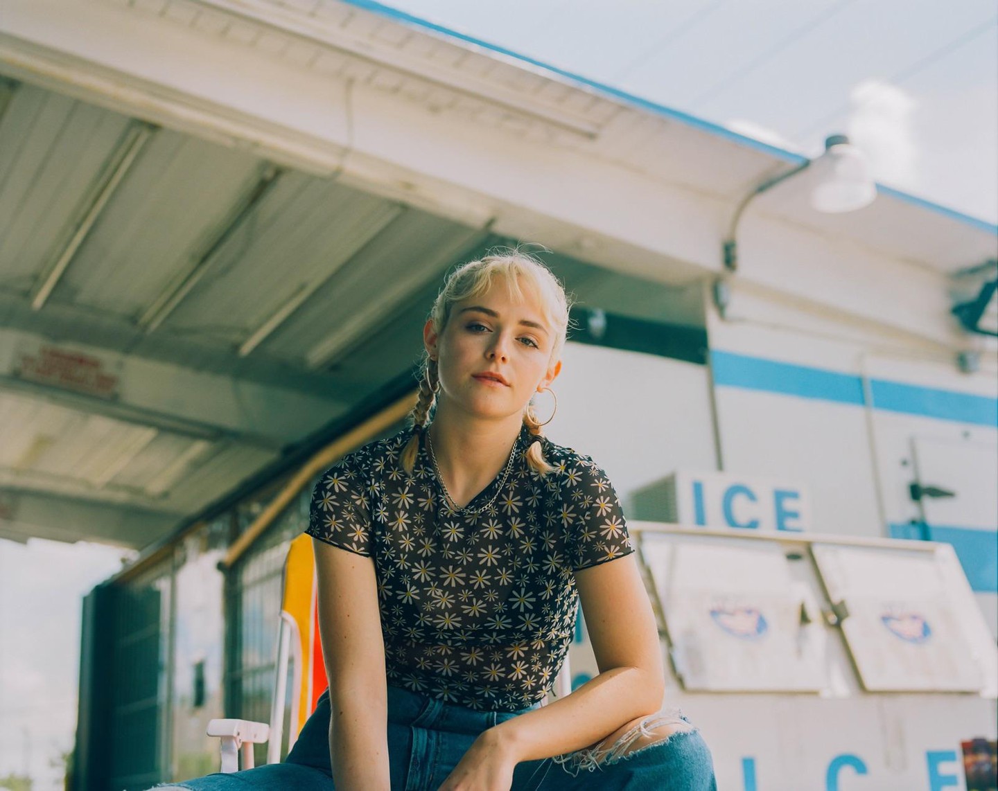 A woman with blonde hair and pigtails sits in front of an ice machine.