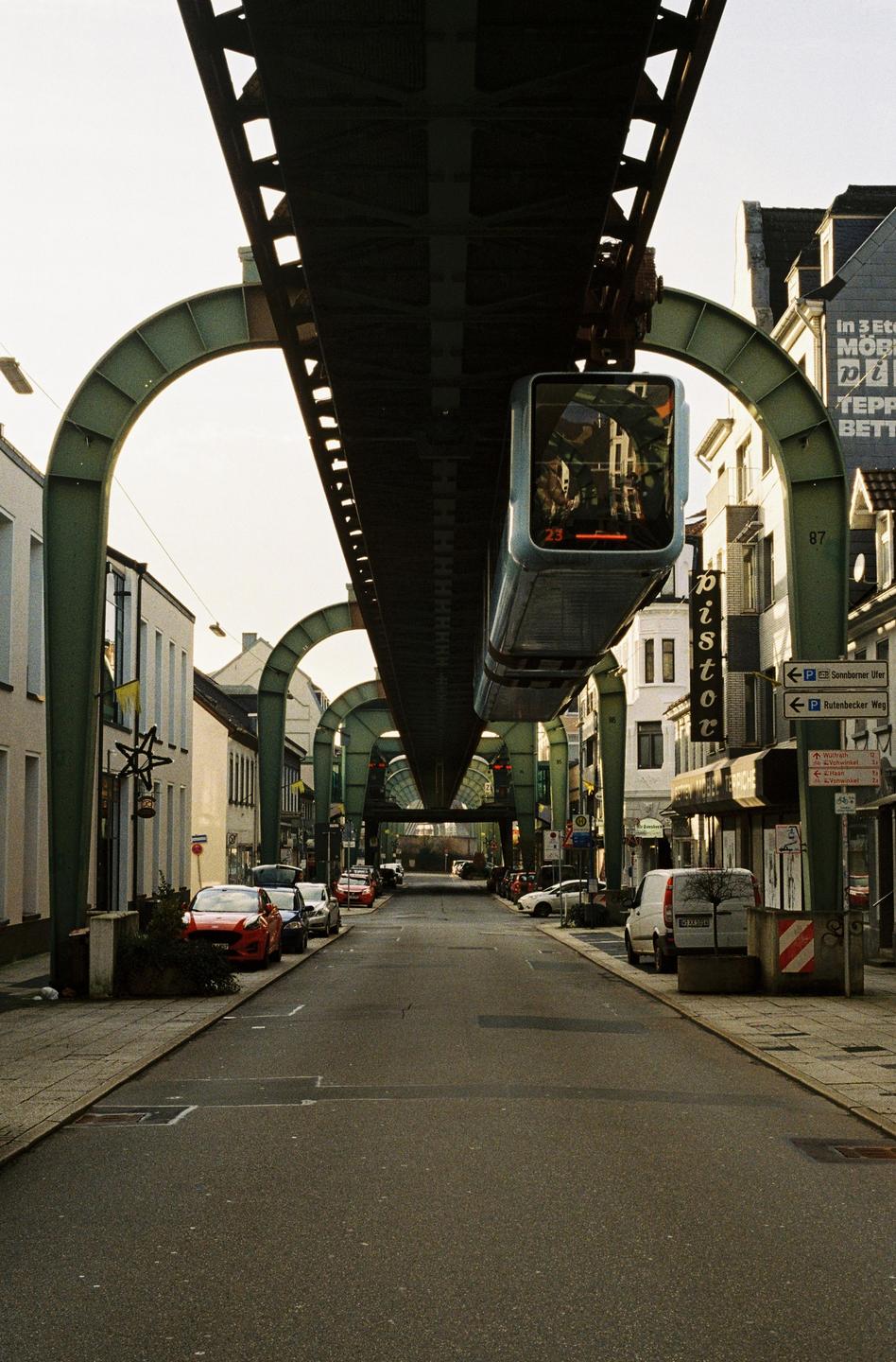 A street in Wuppertal, Germany, is pictured with a suspended monorail train passing overhead.