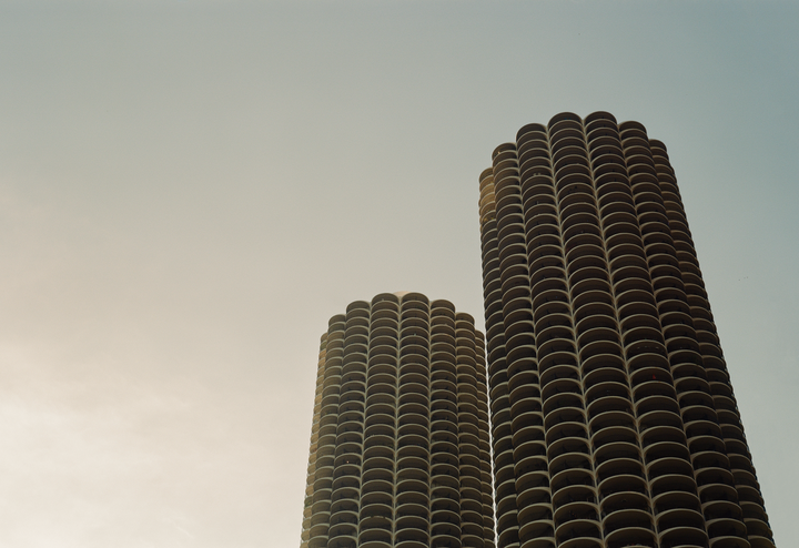 Two cylindrical high-rise buildings with many balconies are visible against a clear sky.