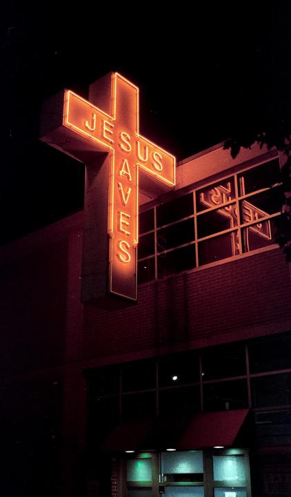 A neon sign in the shape of a cross with the words "Jesus Saves" is illuminated at night.