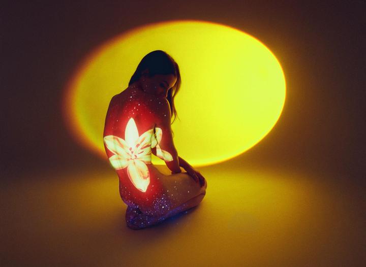A woman kneels with a flower projected onto her back and a large yellow circle projected behind her.