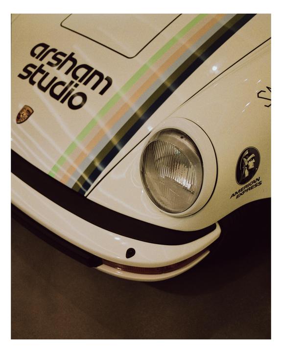 A white Porsche 911 with colorful stripes and "arsham studio" written on the hood is visible.