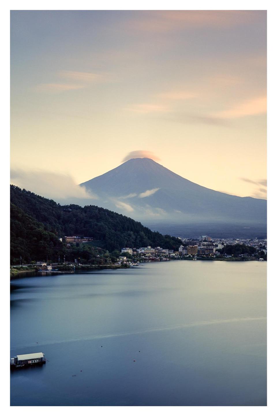 Mount Fuji rises above a town and a lake with a small boat.