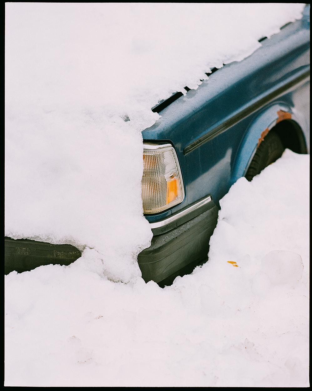 A blue car is partially covered in snow.