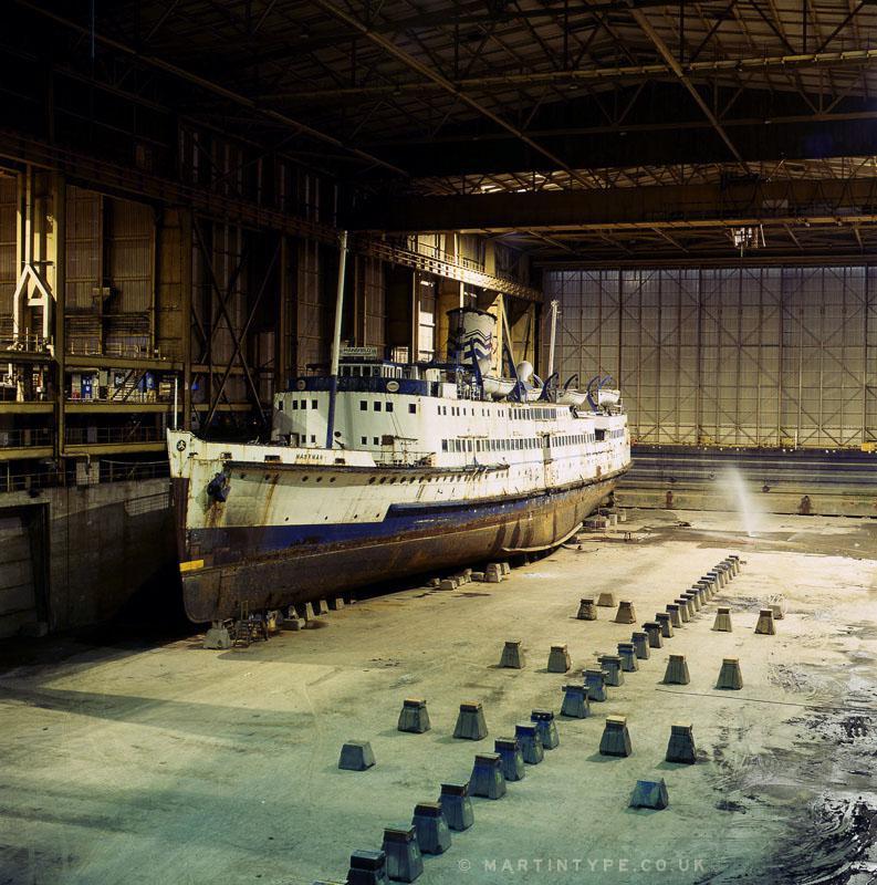 A large ship sits in a dry dock with rows of concrete blocks on the ground.
