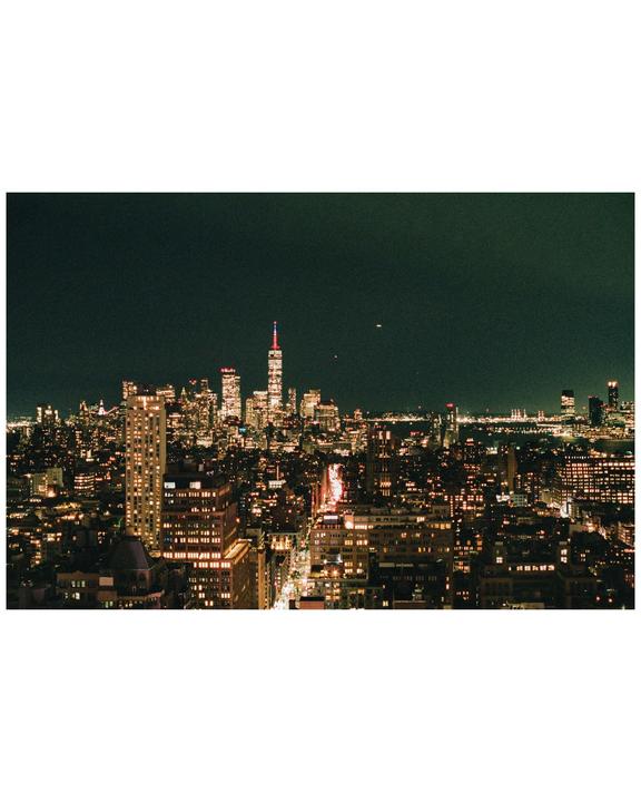 A city skyline is illuminated at night with a prominent skyscraper in the distance.
