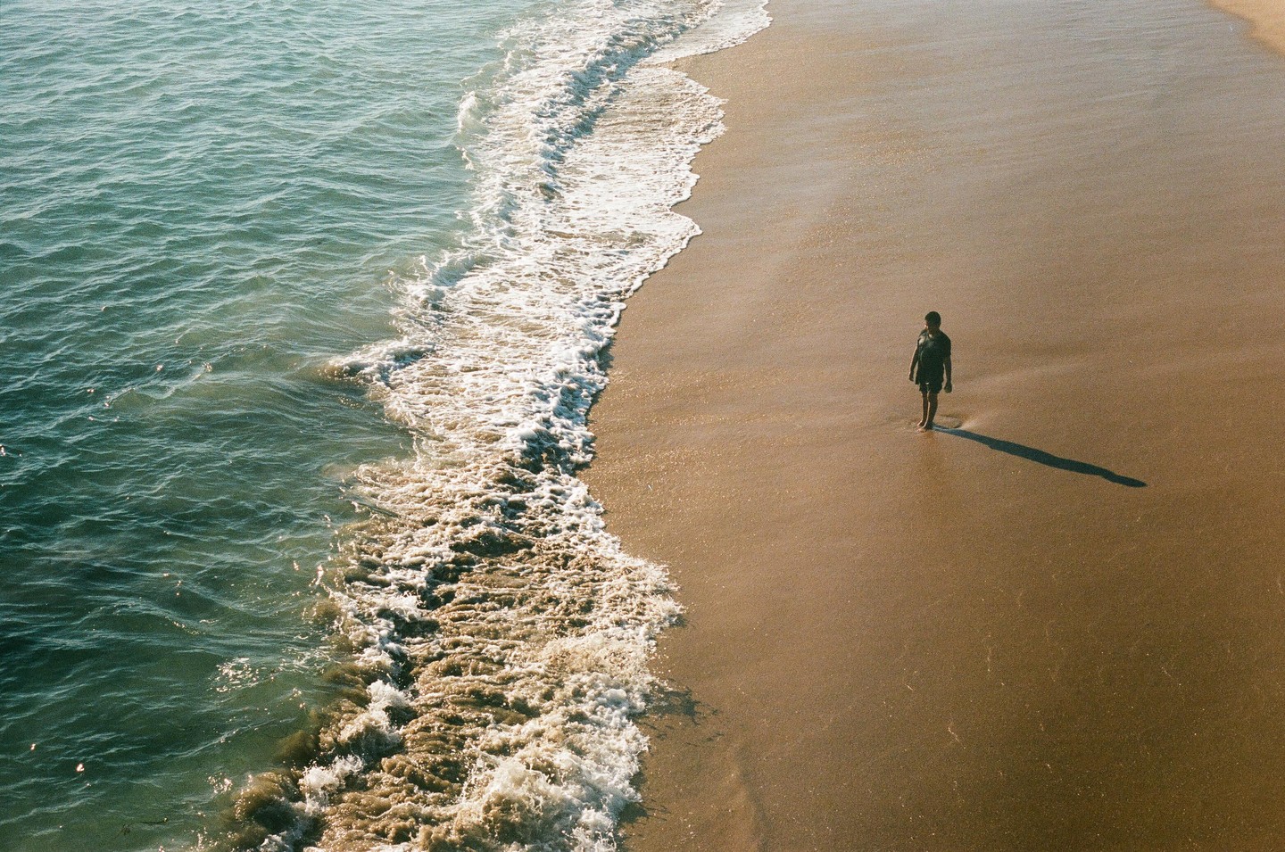 A person stands on a sandy beach next to the ocean waves.
