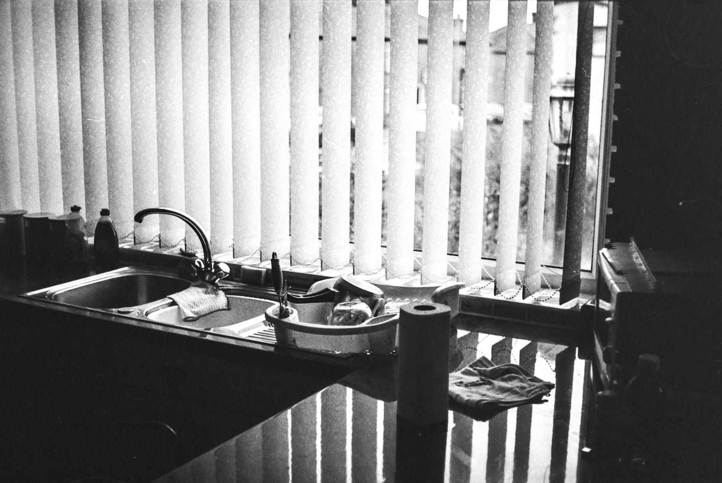 A kitchen sink and counter are visible in front of a window with vertical blinds.