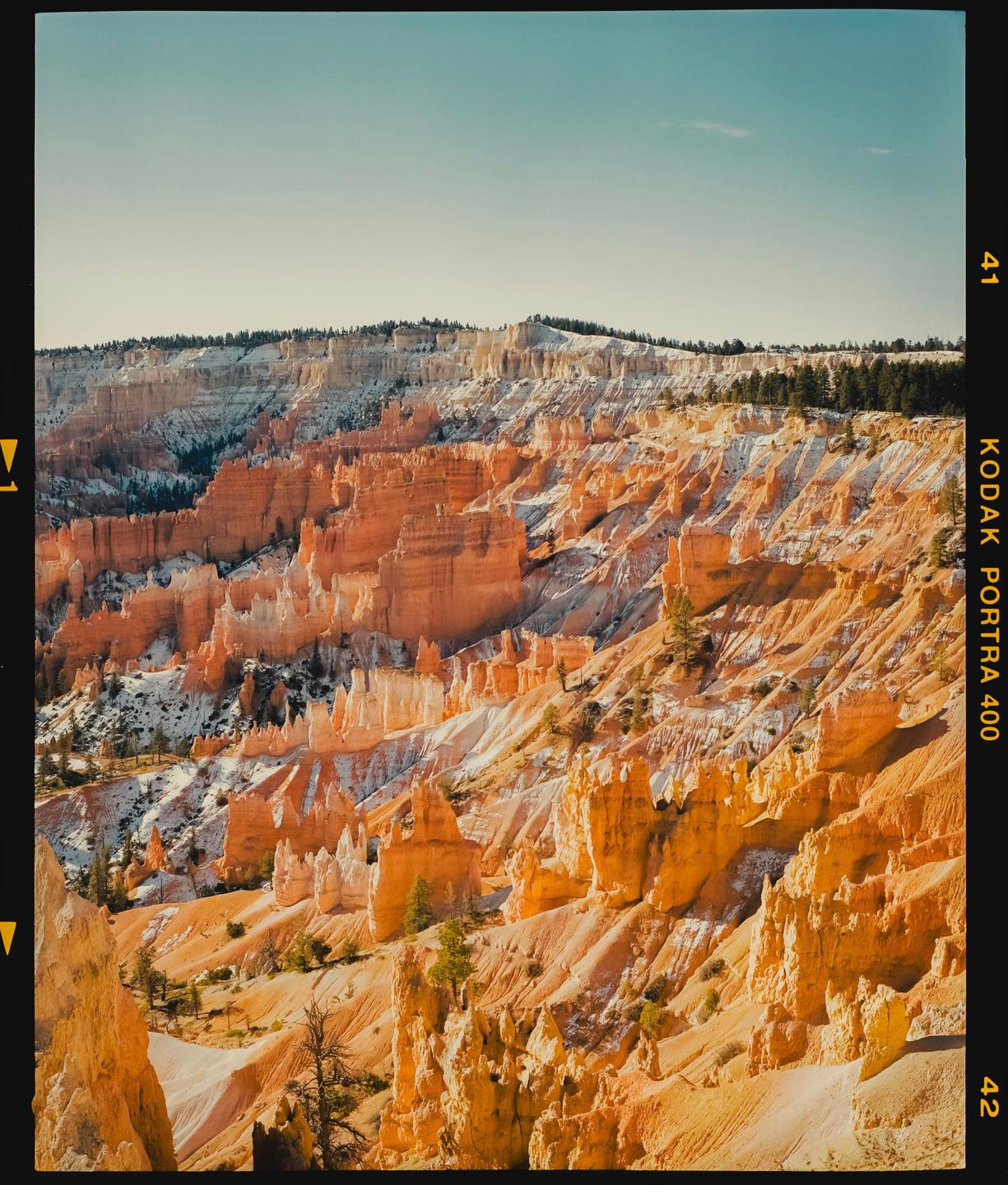 A vast canyon landscape features orange and white rock formations under a clear sky.
