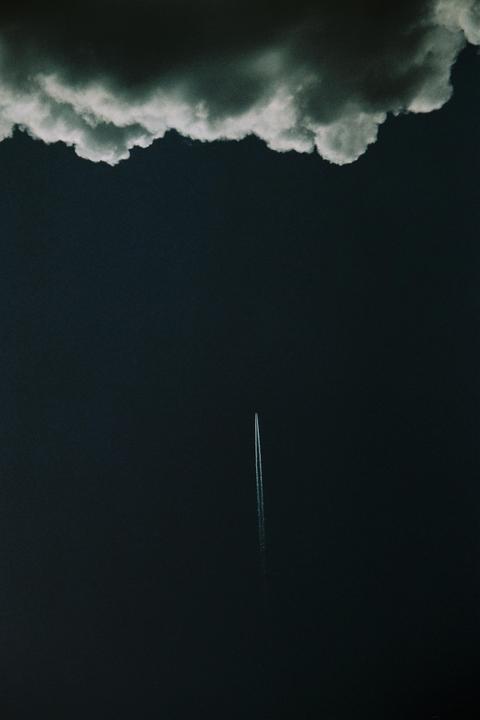 A single airplane contrail streaks across a dark sky with a cloud formation at the top.