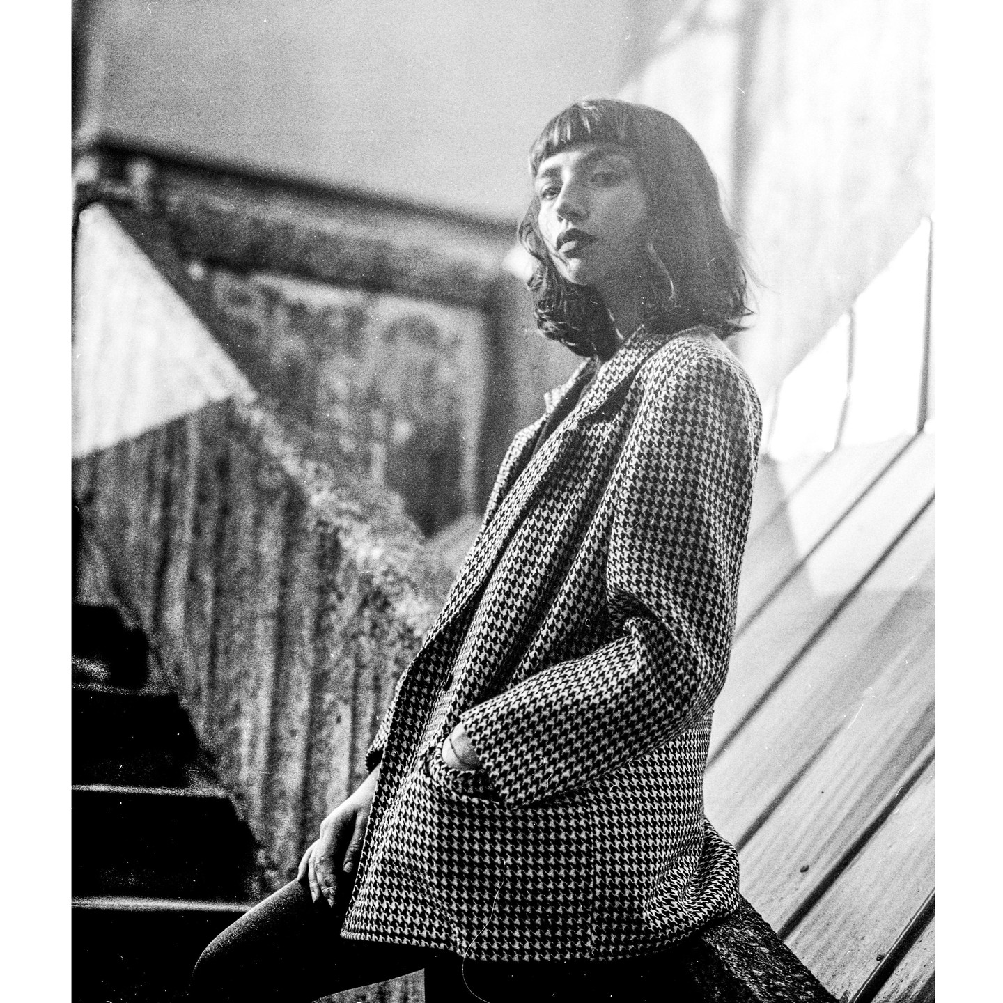 A woman in a houndstooth jacket stands on a staircase.