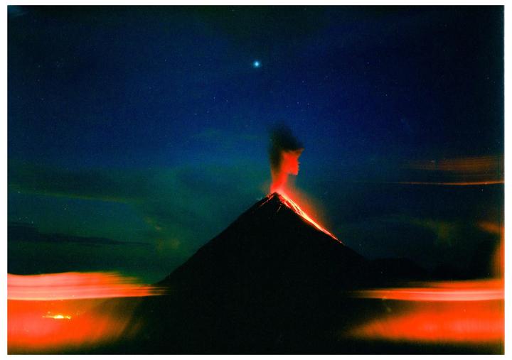 A volcano erupts at night, spewing lava down its side and smoke into the starry sky.