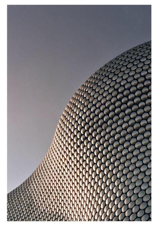 The facade of a modern building covered in metallic discs curves against a gray sky.