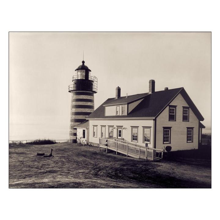 A lighthouse with horizontal stripes stands next to a house with a ramp leading to its entrance.