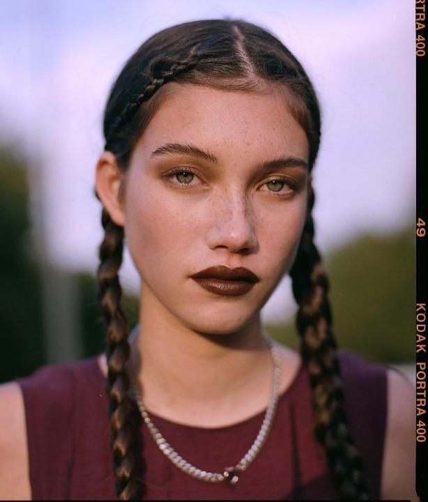 A woman with braided hair and dark lipstick looks directly at the viewer.