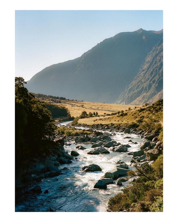 A river with many rocks flows through a valley with mountains in the background.