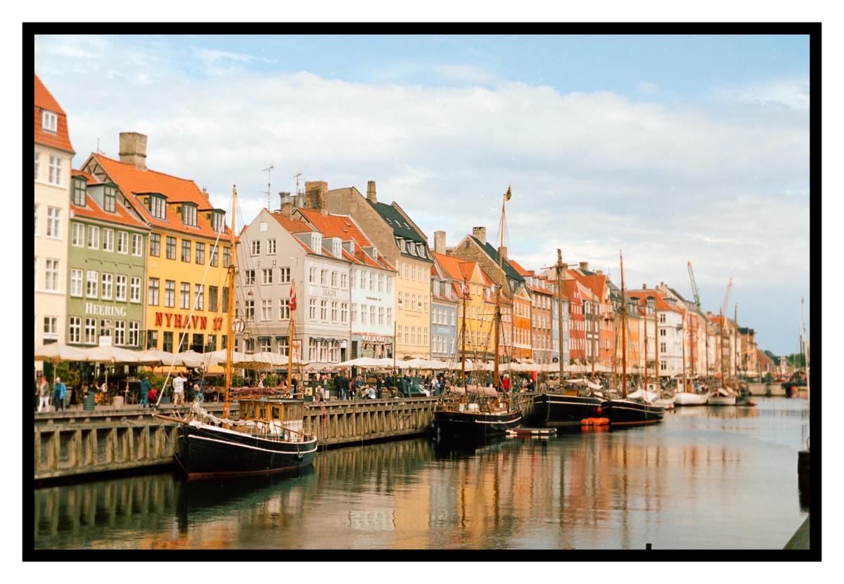A canal is lined with colorful buildings and boats, with people walking along the waterfront.
