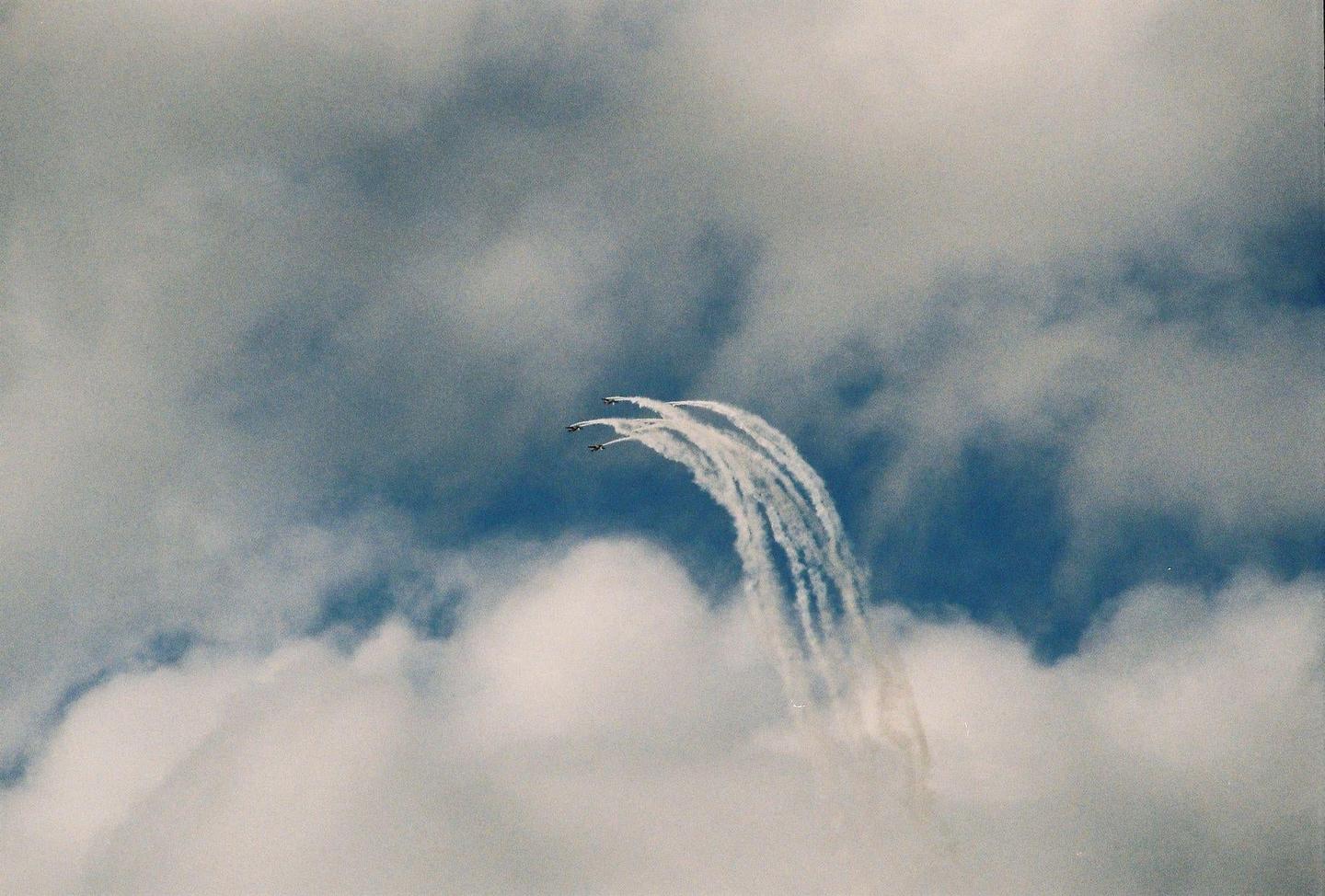 Three airplanes fly in formation, leaving white trails against a blue sky with clouds.