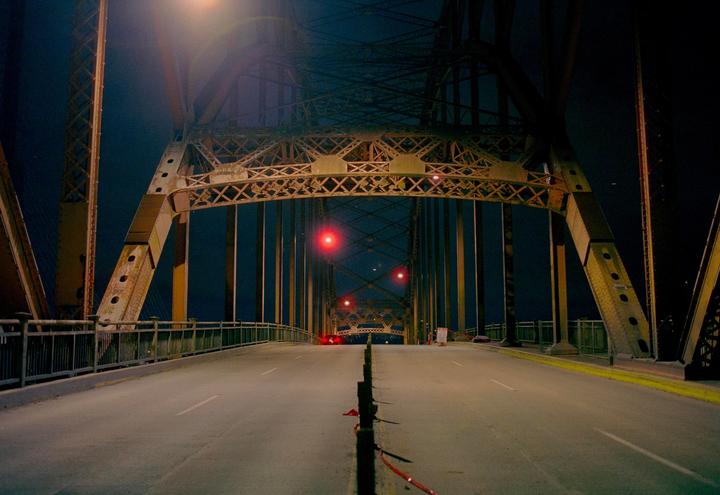 A long exposure shows a bridge at night with red lights in the distance.