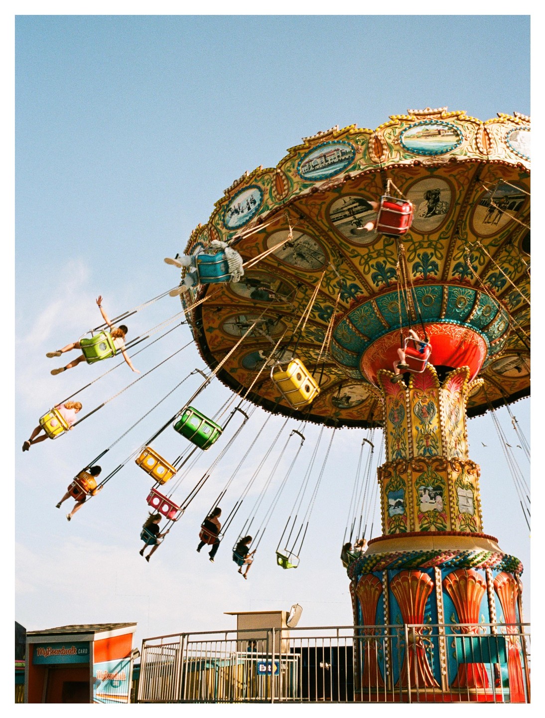 People ride a colorful swing carousel against a clear sky.