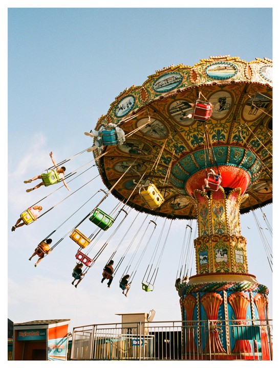 People ride a colorful swing carousel against a clear sky.